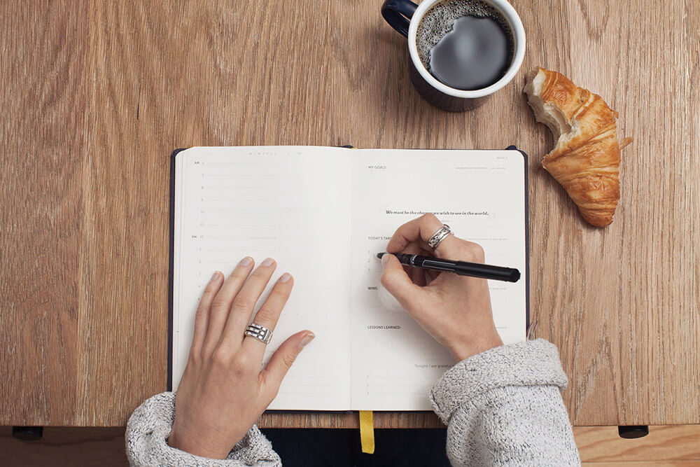 Notebook on a wooden desk with hands holding a pen writing.